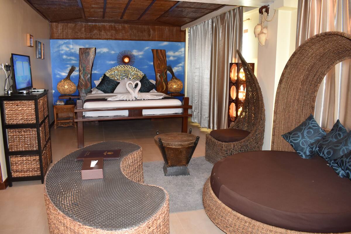 Een kamer met een bed, rieten meubels, een bureau met een computer en een muurschildering.