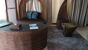 A room with a bed, a round wicker ottoman, a small chair, and a minibar. - Golden Phoenix Hotel Boracay (Boracay Island)