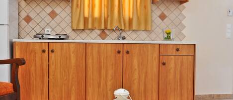 A kitchen with wooden cabinets, a window with yellow curtains, a white lantern, and a table with a wheat bundle.