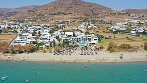 A coastal town with white buildings, a beach, and a mountain in the background. - Akti Aegeou Hotel (Tinos)