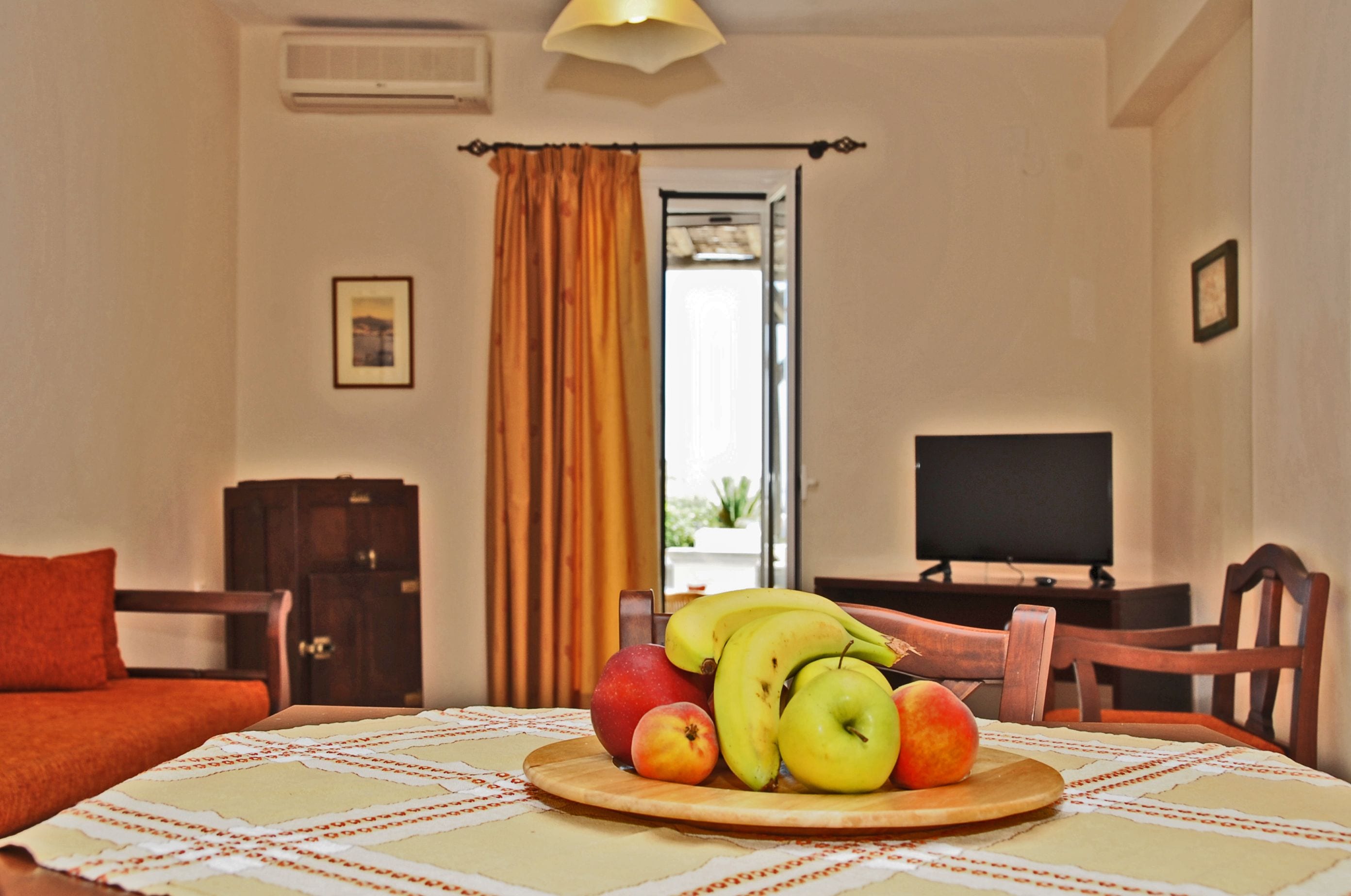 A dining table with a fruit platter, a television, and a view of the outdoors through a window.