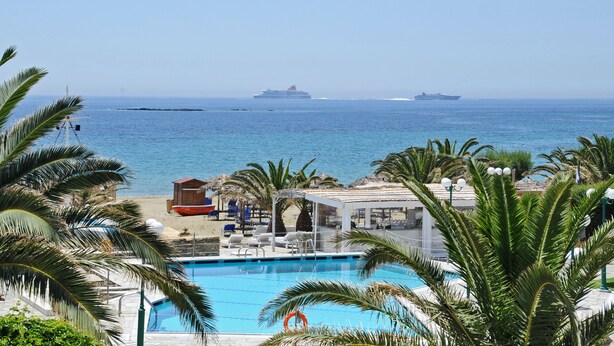 A pool area with lounge chairs and umbrellas, overlooking the sea with cruise ships in the distance. - Akti Aegeou Hotel (Tinos)