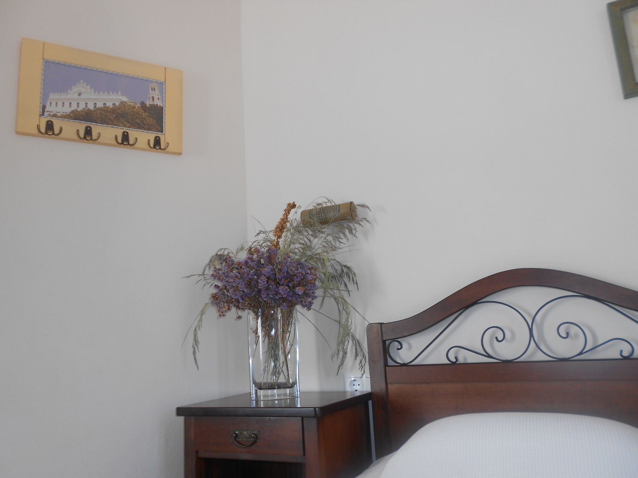 A bedroom with a wooden headboard, a bedside table with a vase of flowers, and a framed picture on the wall.