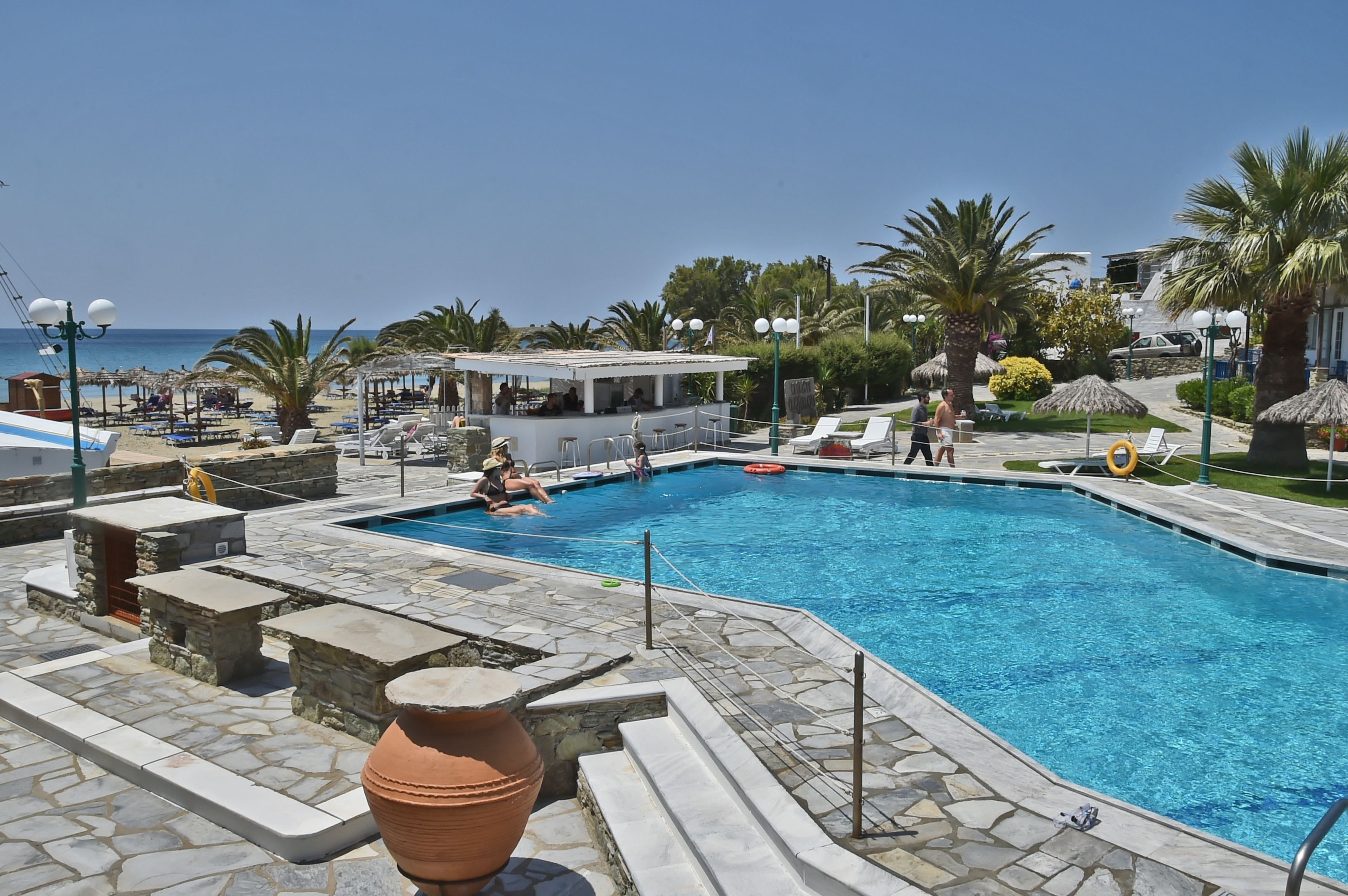 A swimming pool with lounge chairs and umbrellas, a bar area, and a view of the sea.