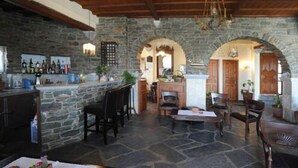 A stone-floored interior with a bar area, wooden furniture, and arched doorways. - Akti Aegeou Hotel (Tinos)