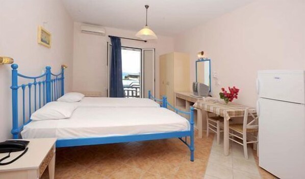 Una habitación con cama, escritorio, silla, espejo y refrigerador.