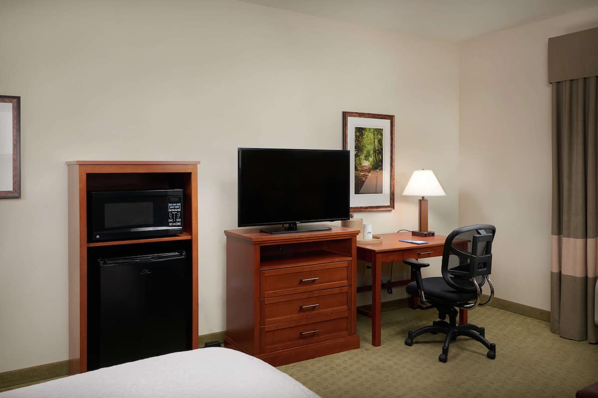 A hotel room with a bed, a desk with a computer, a television, a microwave, and a small refrigerator.