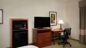 Habitación de hotel con cama, escritorio con computadora, televisor, microondas y refrigerador pequeño.