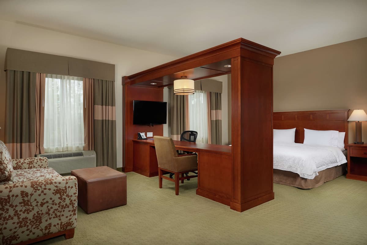 A hotel room with a bed, a desk, a chair, a television, and a large window with curtains.