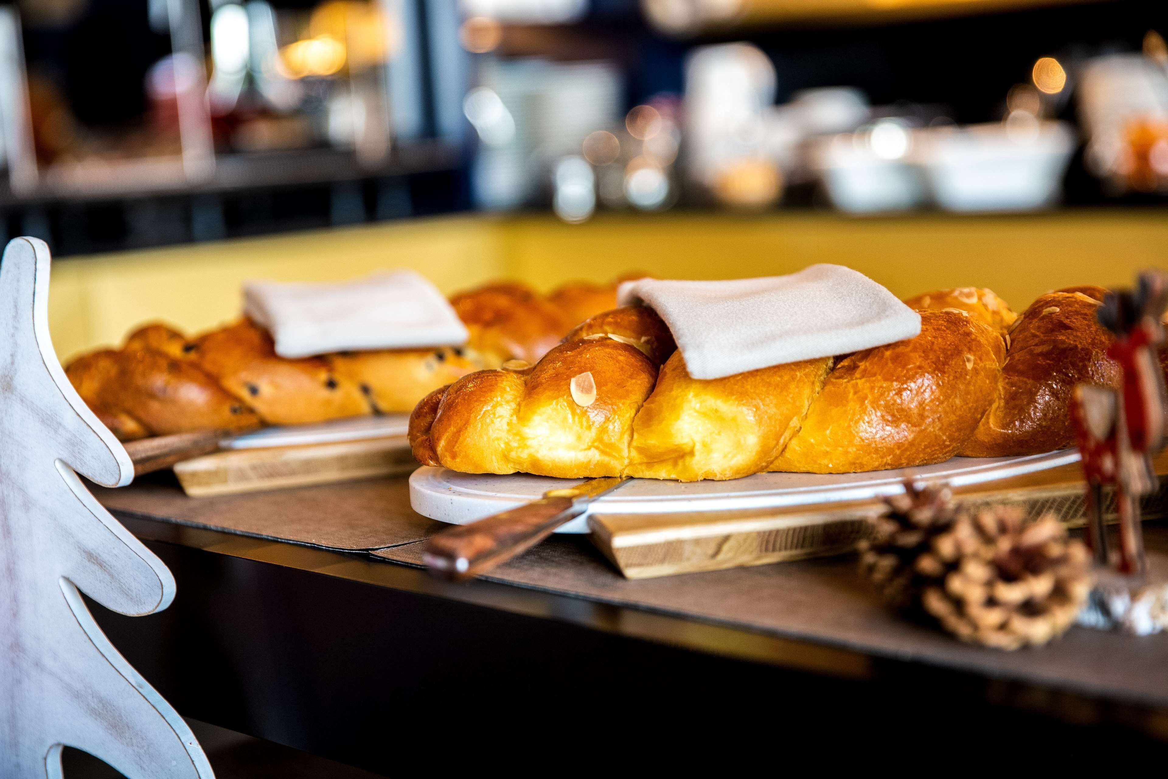 A bakery display with various breads and pastries, a knife, and a pine cone on a table.