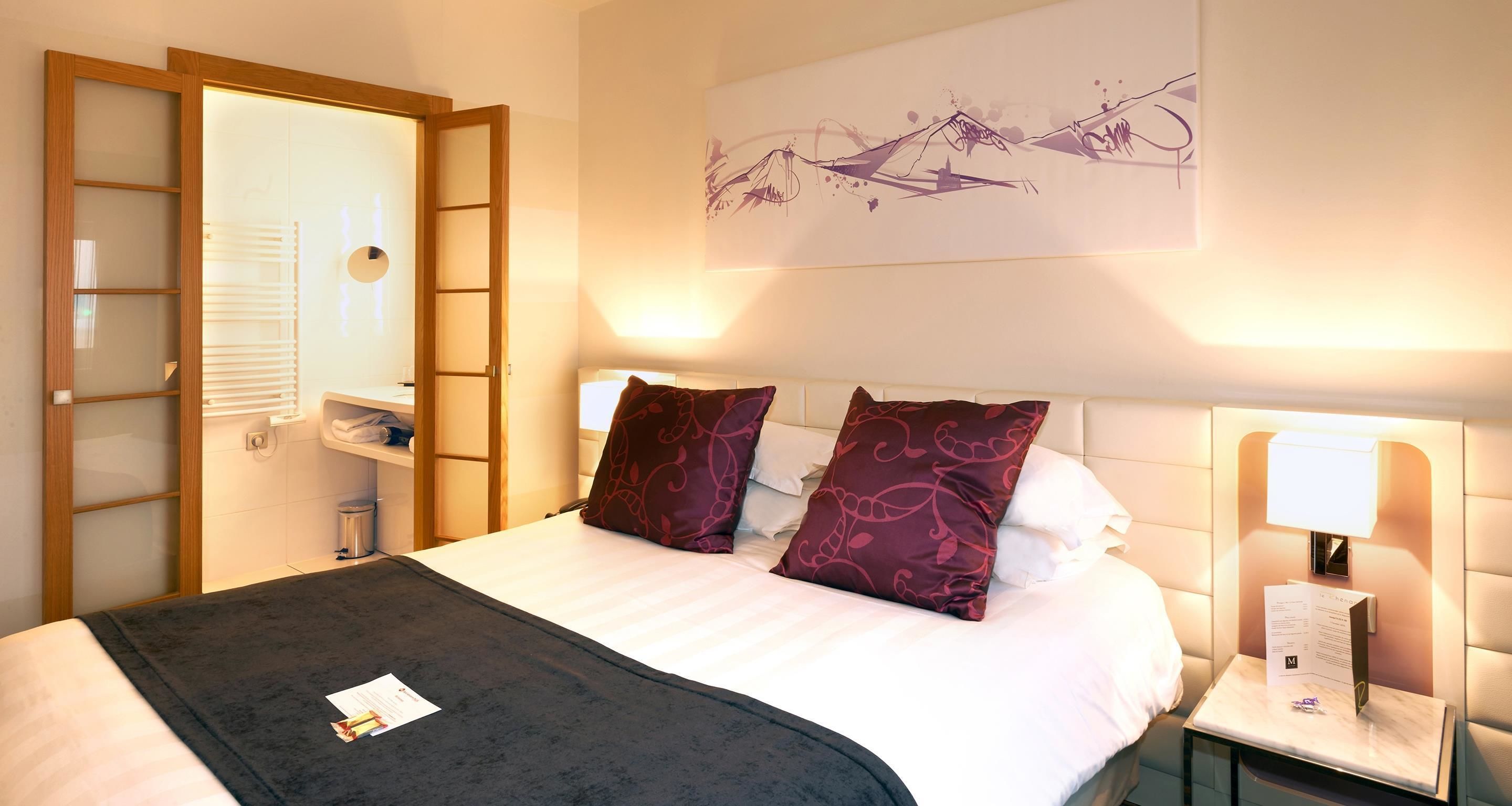Quarto de hotel com cama, mesa de cabeceira, espelho e obra de arte na parede.