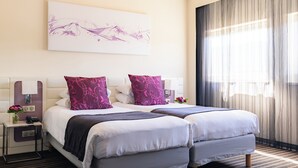 A hotel room with two beds, a bedside table with a lamp, a phone, and a vase with flowers.