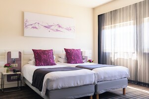 A hotel room with two beds, a bedside table with a lamp, a phone, and a vase with flowers.