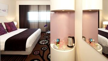 A hotel room with a bed, bedside table, and a window with curtains.