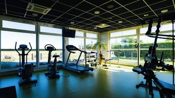 Un gimnasio con diverso equipo de ejercicio, ventanas amplias y vistas al exterior a zonas verdes.
