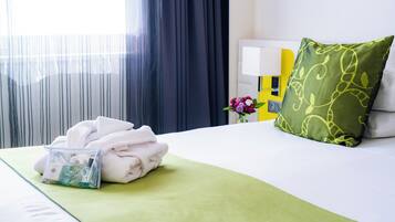 A neatly made bed with a green bedspread, a pillow with a leaf pattern, and a small bag of toiletries on the side.