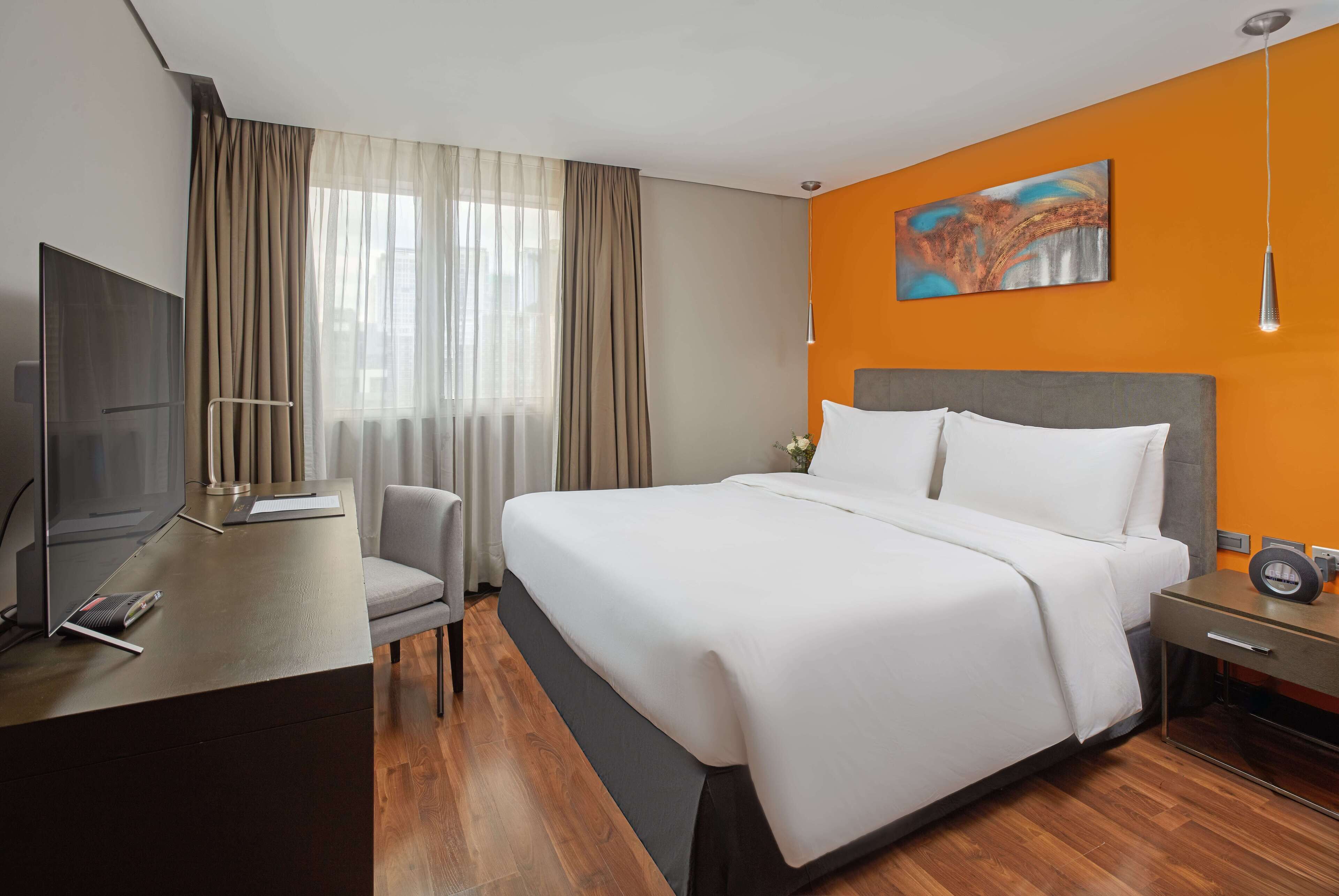 Een hotelkamer met een groot bed, een bureau met een televisie en een schilderij aan de muur.