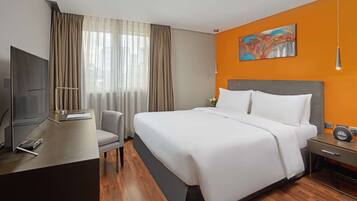 Habitación de hotel con una cama grande, un escritorio con televisor y un cuadro en la pared.