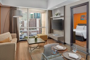 Una habitación de hotel moderna con un ventanal grande, un sofá, una mesa de comedor y una cama.