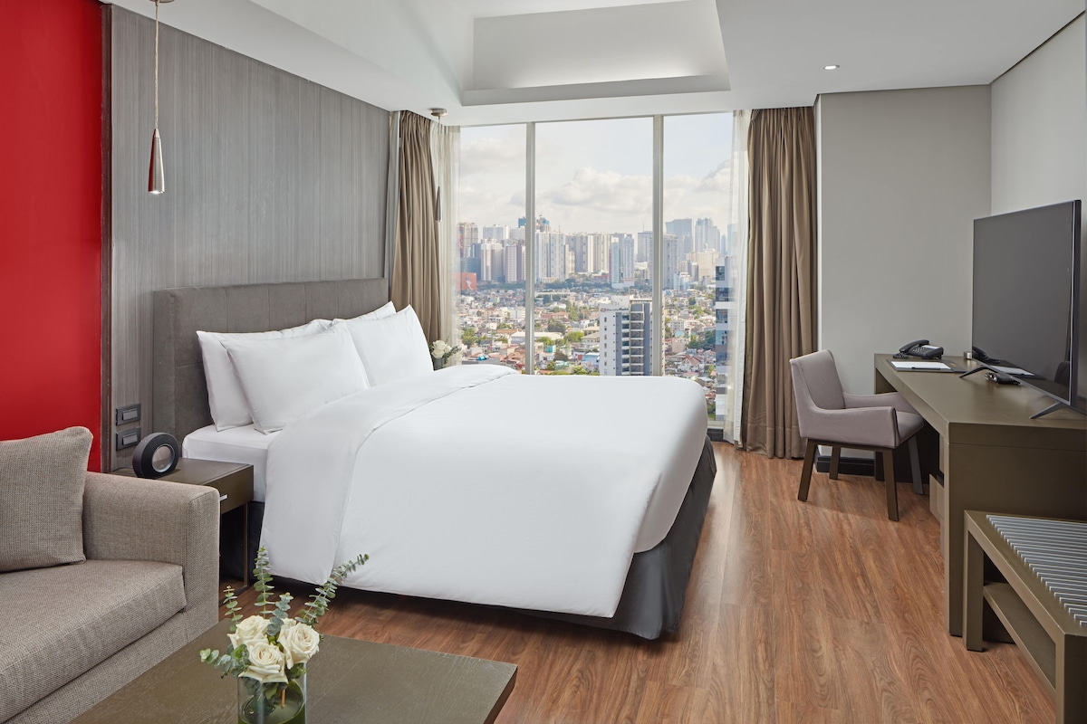 Una habitación de hotel moderna con una cama grande, un escritorio y vistas a la ciudad.
