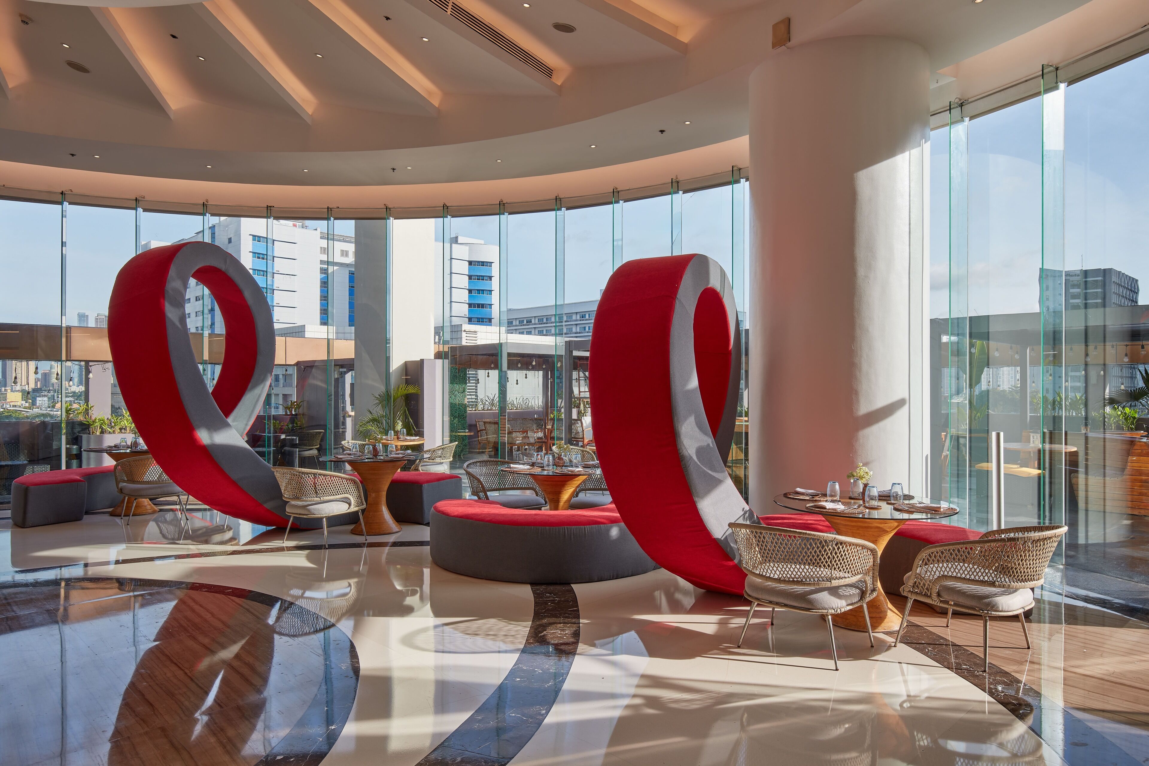 Eine moderne Lobby mit Glaswand, runden Sitzbereichen und einem zentralen Tisch mit Stühlen.