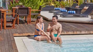 A couple sitting by a poolside with lounge chairs and wooden deck.