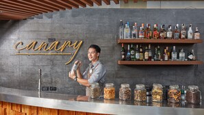 A bar area with a wooden counter, a man holding a cocktail shaker, and shelves with various liquor bottles. - F1 Hotel Manila (Taguig)