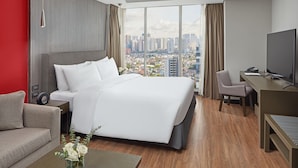 A modern hotel room with a large bed, a desk, and a view of the cityscape. - F1 Hotel Manila (Taguig)