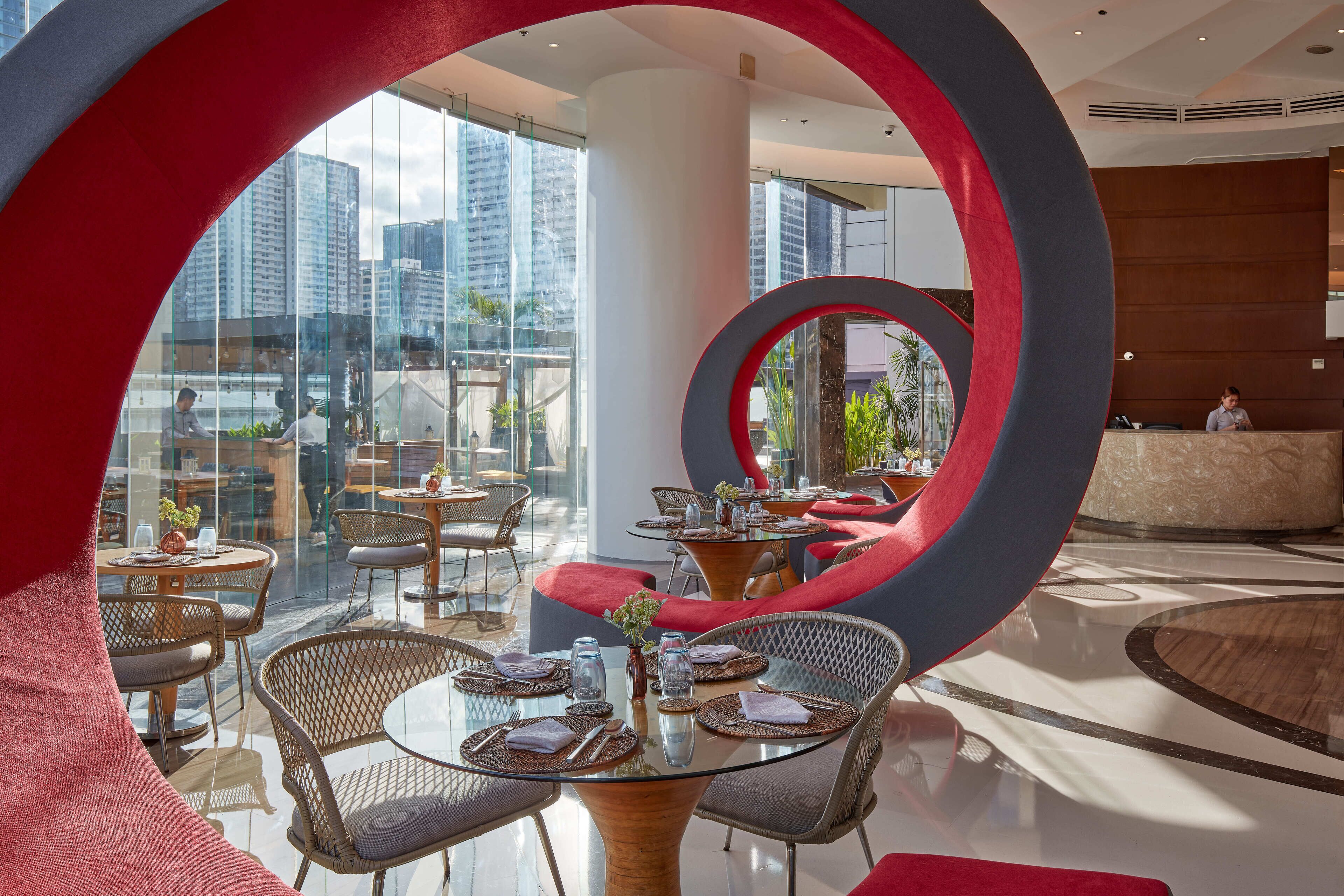 A modern hotel lobby with glass walls, red circular decor, and a reception desk.
