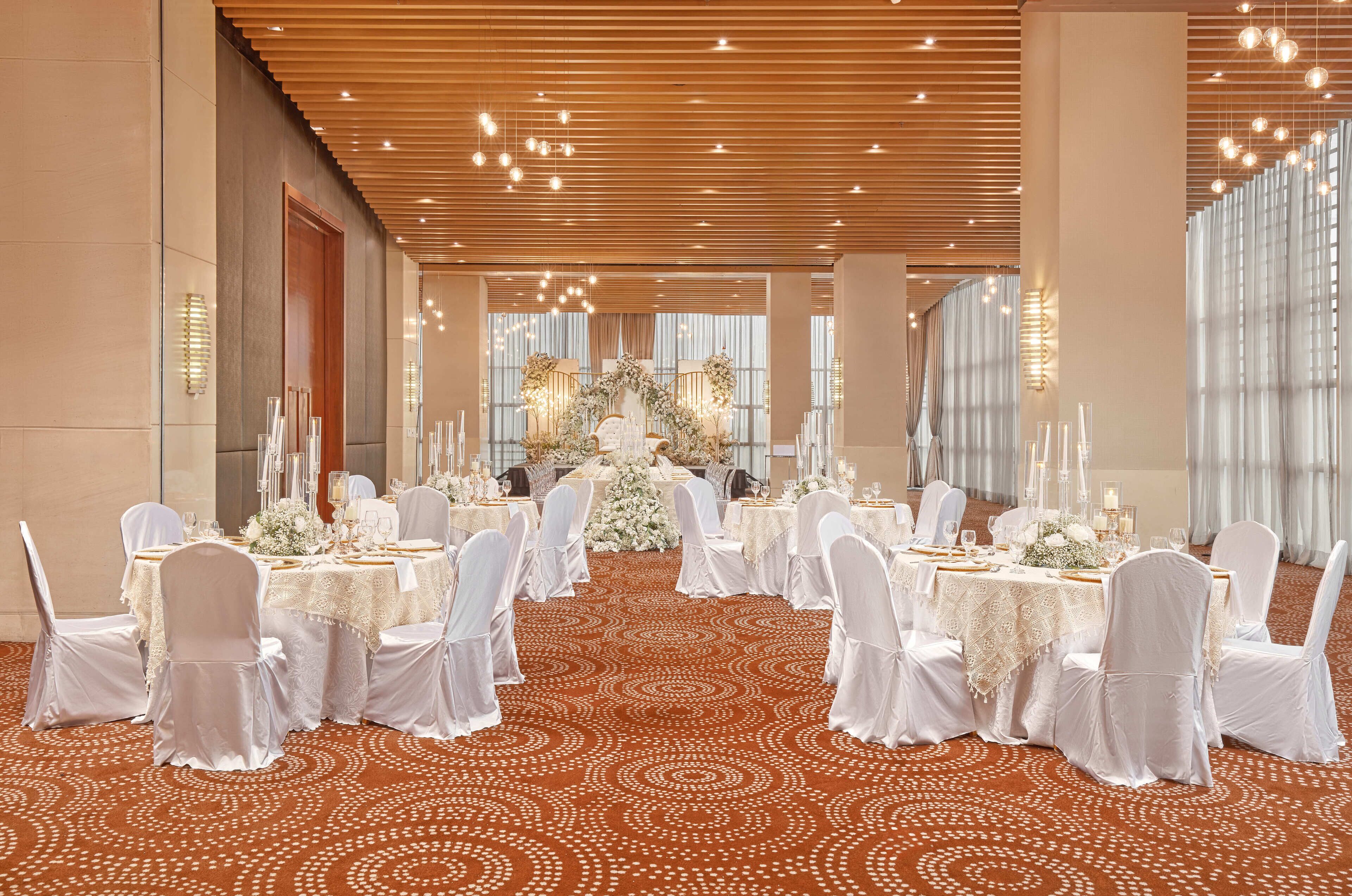 A banquet hall with round tables, white chairs, and a patterned carpet.