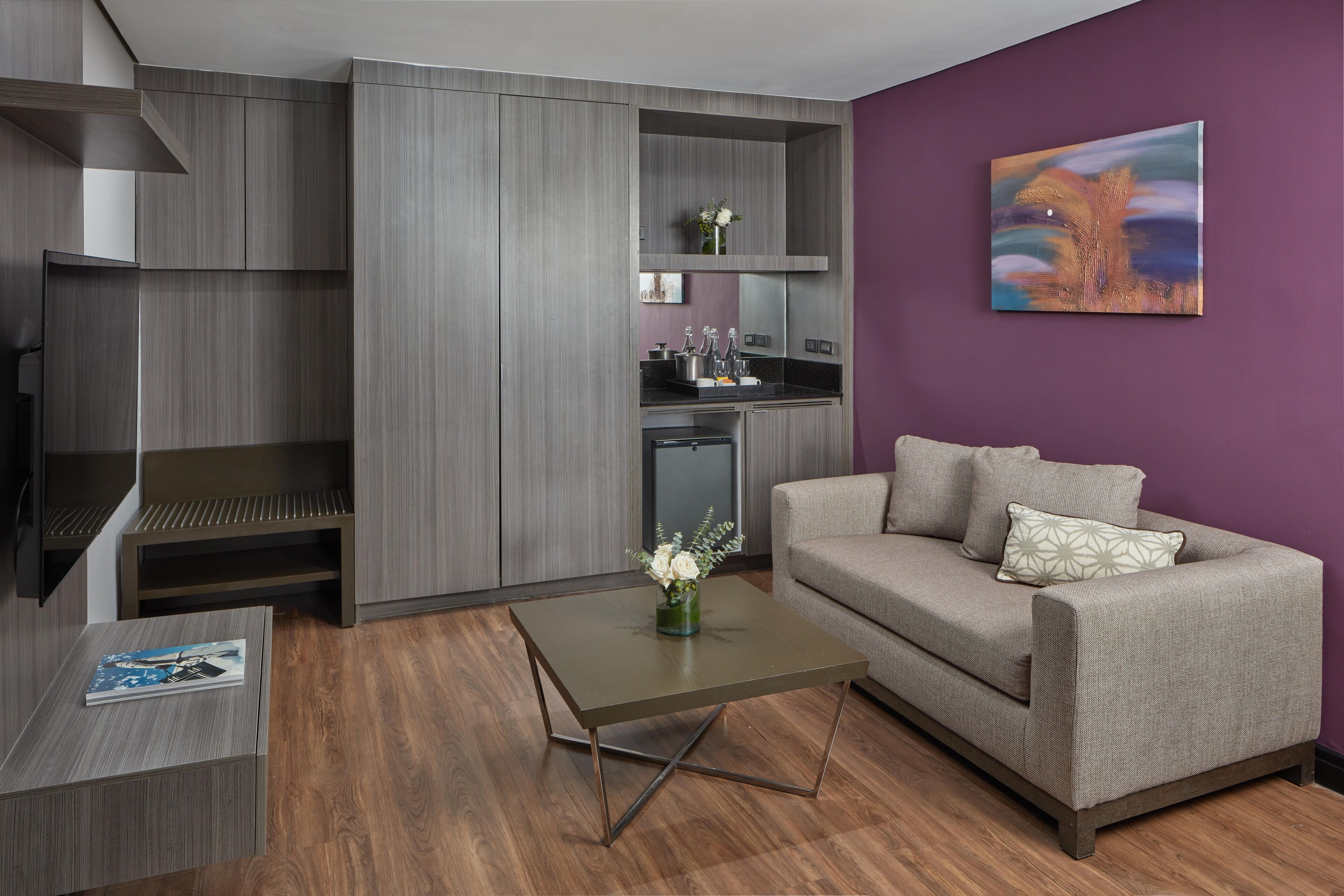 A modern living room with a grey sofa, a coffee table, and a kitchen area with grey cabinets.