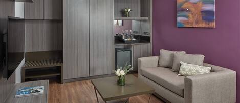 A modern living room with a grey sofa, a coffee table, and a kitchen area with grey cabinets.