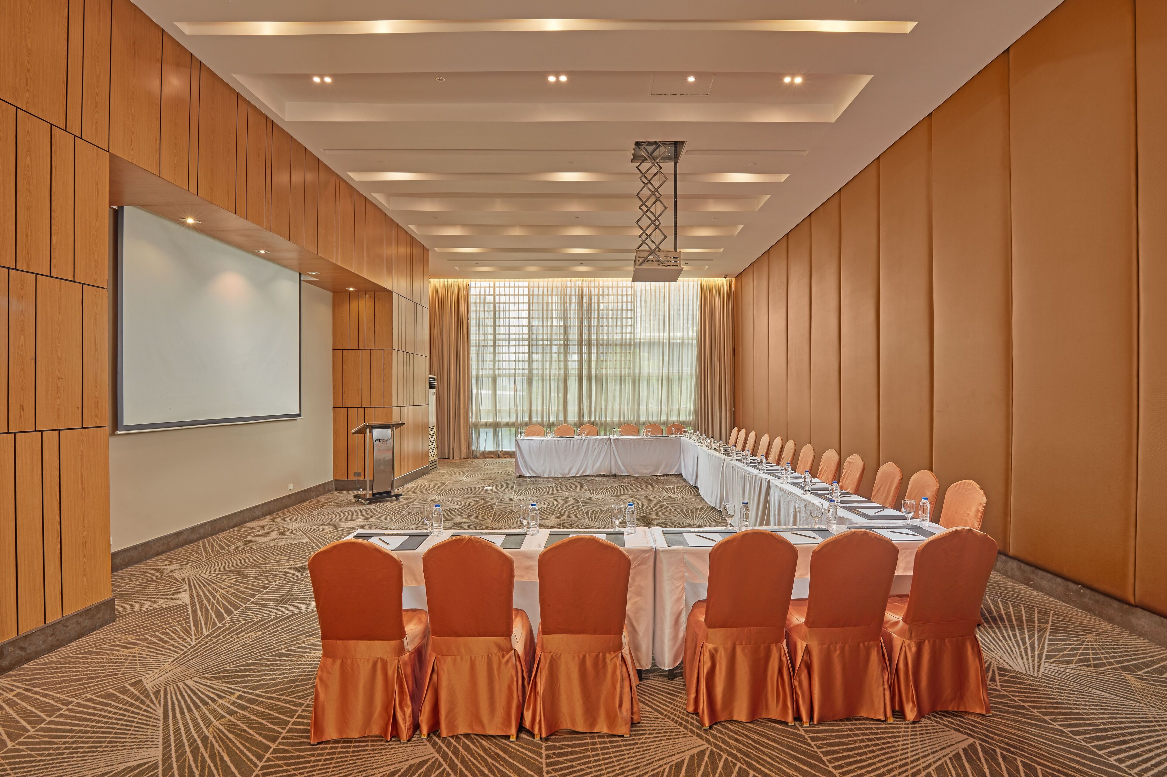A conference room with a long table, orange chairs, and a projector screen.