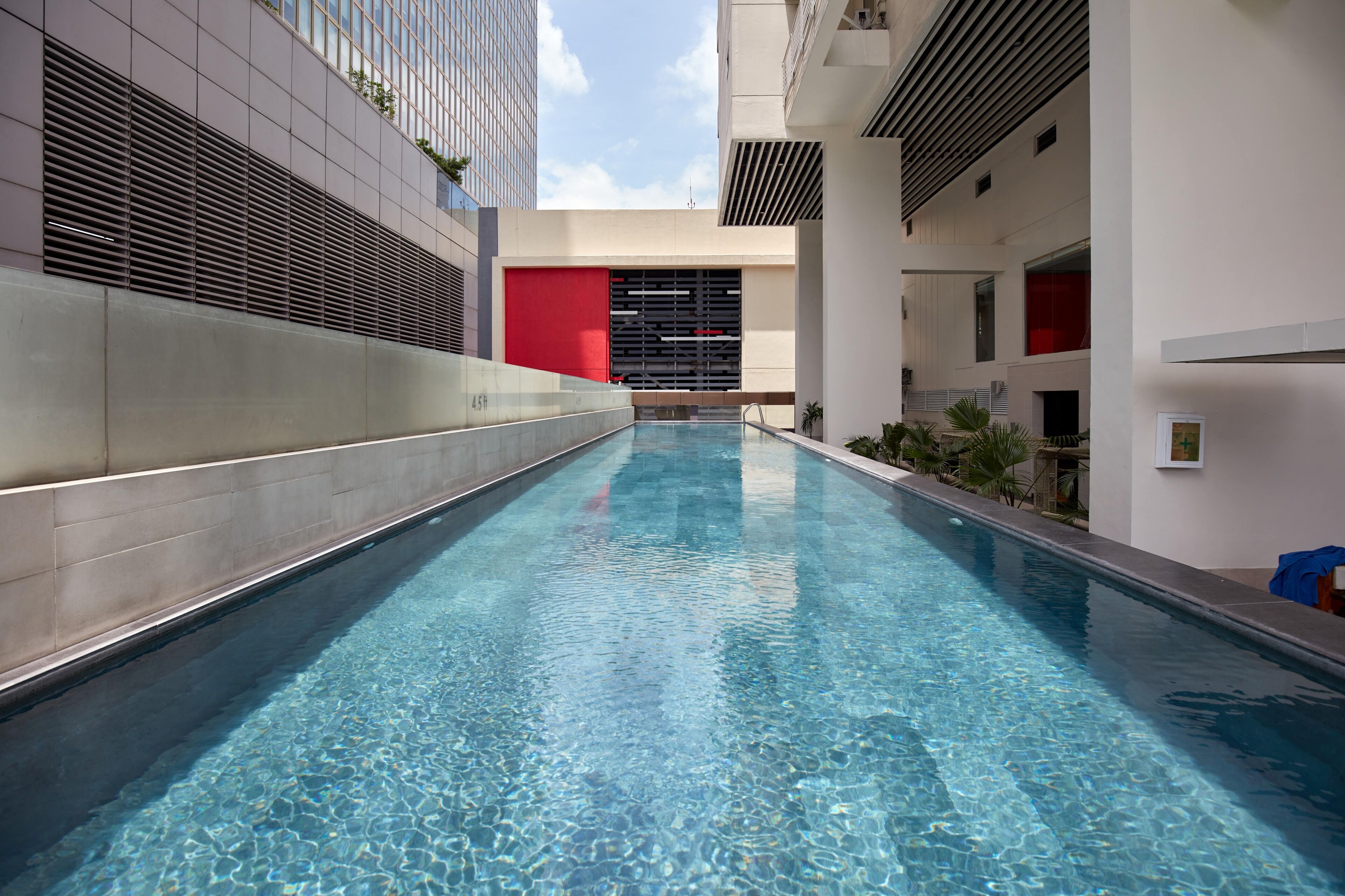 Piscina interna moderna com água cristalina, cercada por um design arquitetônico minimalista com uma parede de destaque vermelha e vista para o céu.