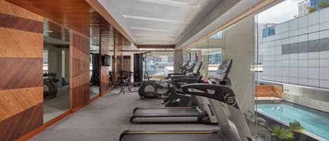 Un gimnasio moderno con cintas de correr, bicicletas estáticas y una zona de piscina visible a través de amplias ventanas.