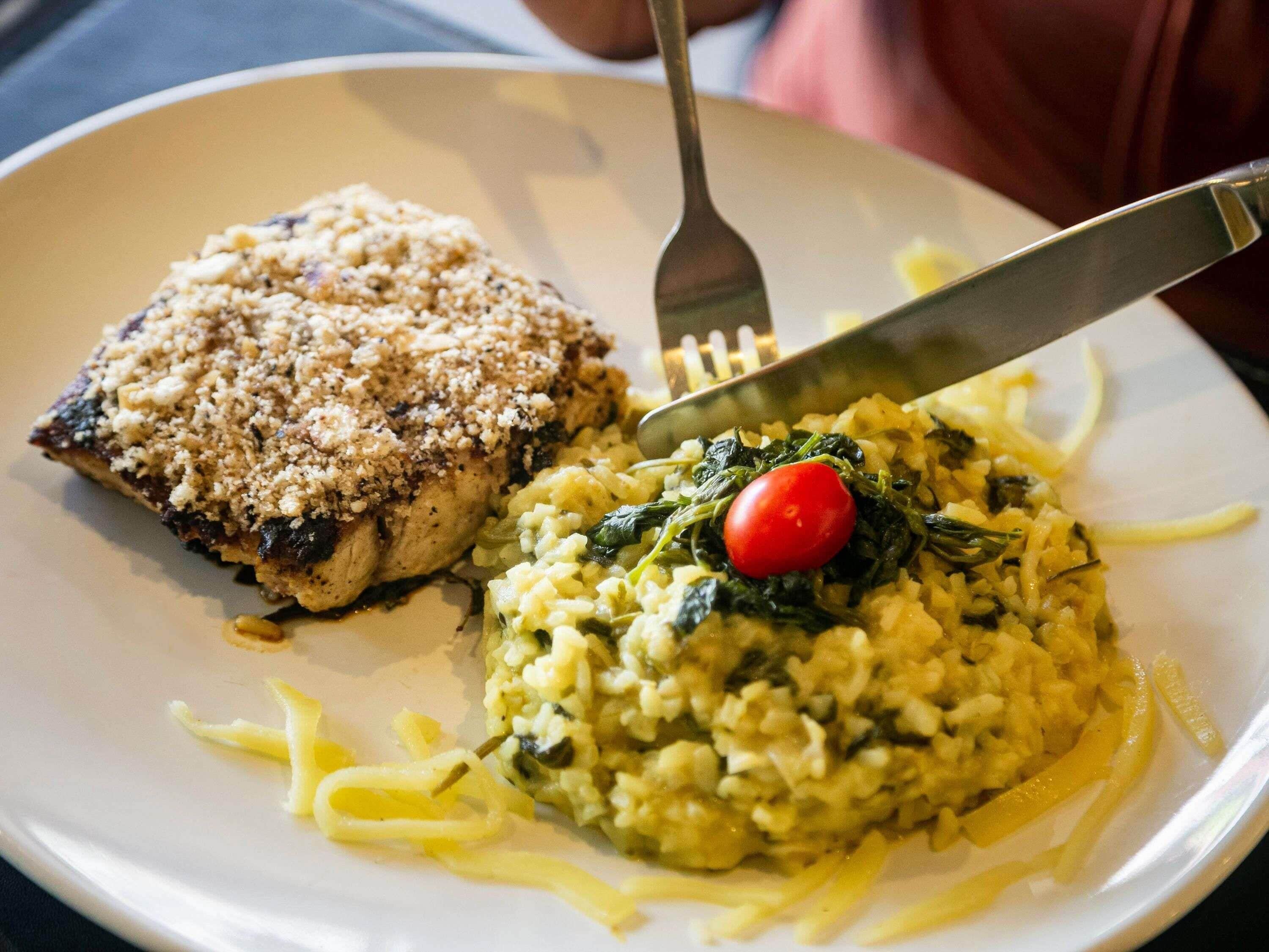 A plate with a piece of breaded chicken and a serving of risotto with spinach and a cherry tomato.