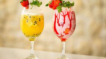 Two cocktails in stemmed glasses, one with a yellow base and the other with a red base, both garnished with a strawberry and mint leaves.
