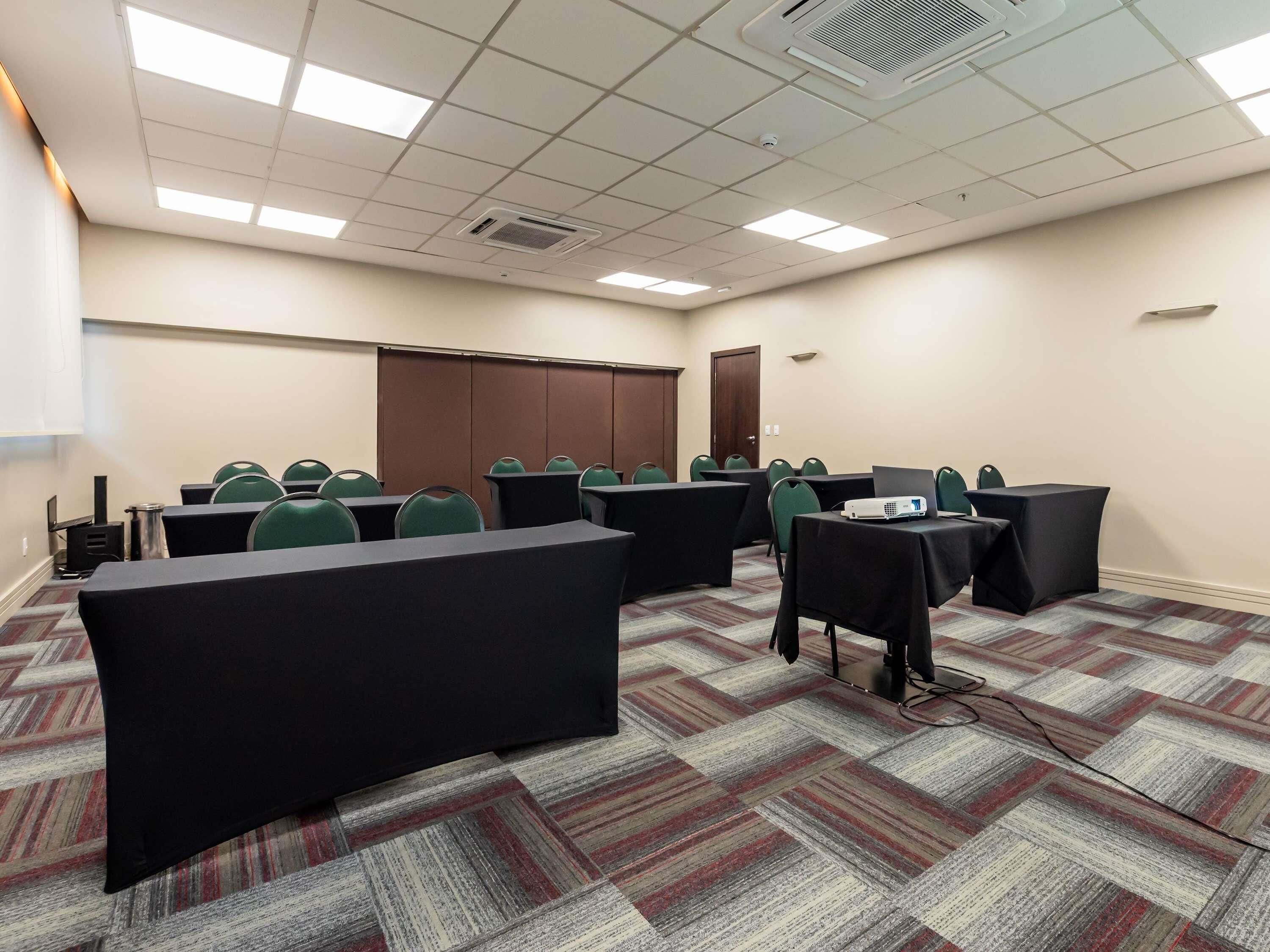 Un salón de conferencias con mesas, sillas, un proyector y piso alfombrado.