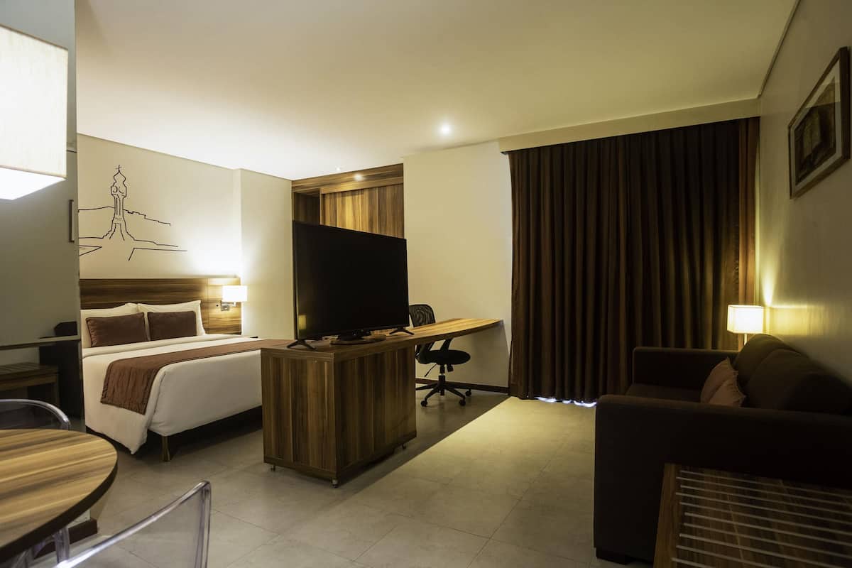A hotel room with a bed, desk, TV, and a couch.