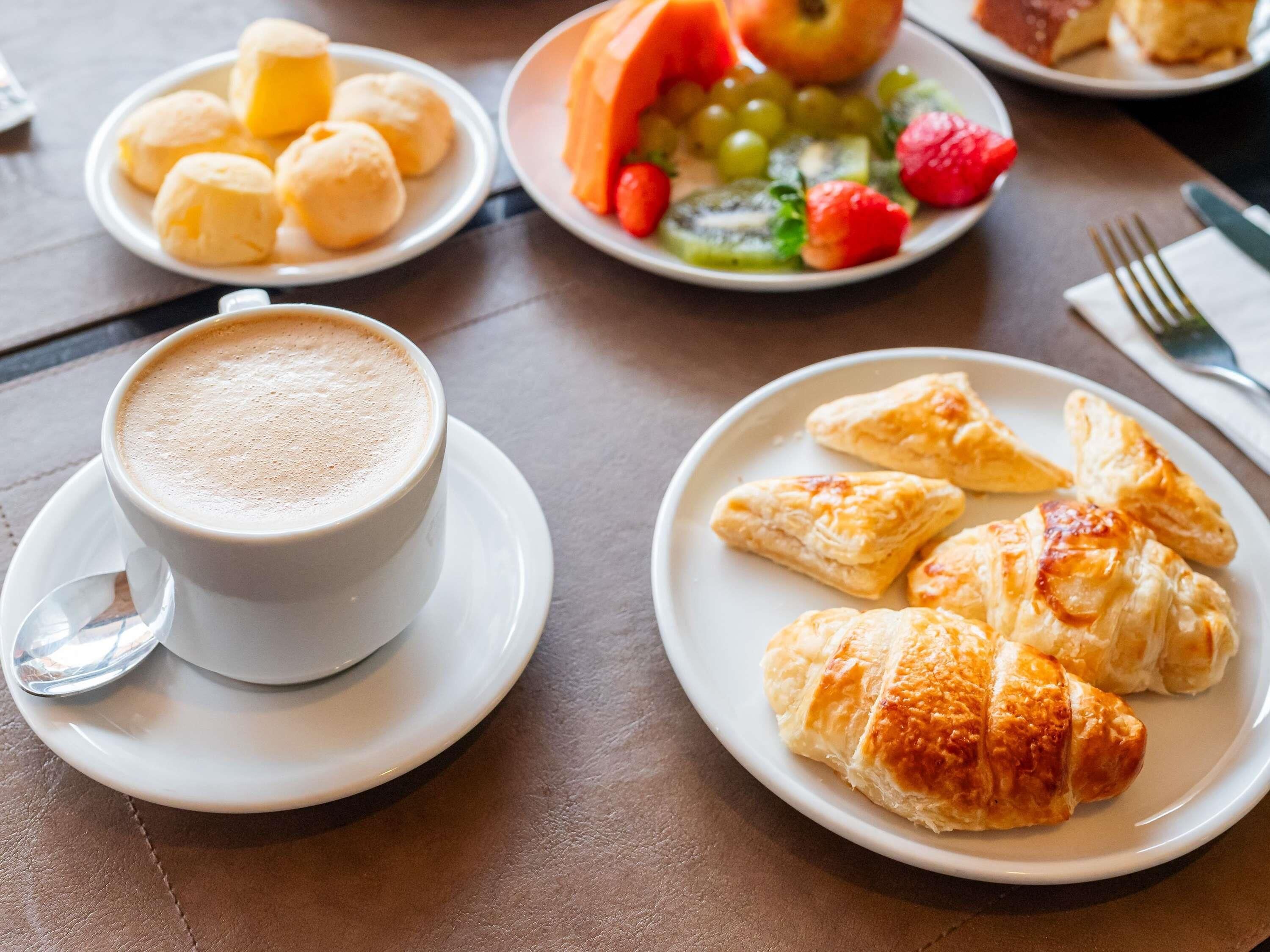 Una mesa con una taza de café, croissants y una bandeja de fruta.