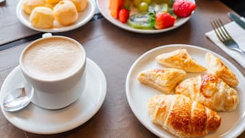 Una mesa con una taza de café, croissants y una bandeja de fruta.