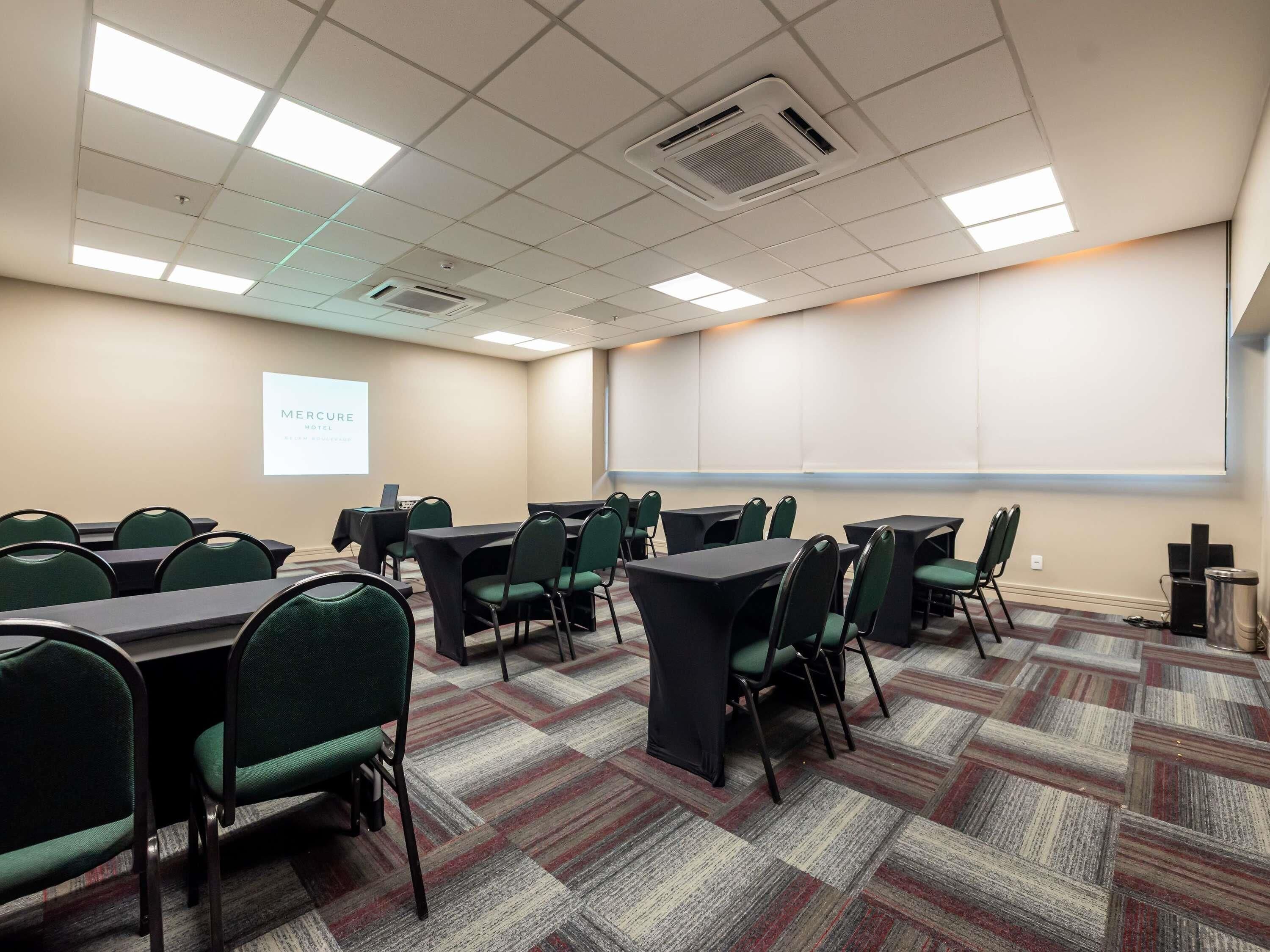 Un salón de conferencias con mesas y sillas, una pantalla de proyector y piso alfombrado.