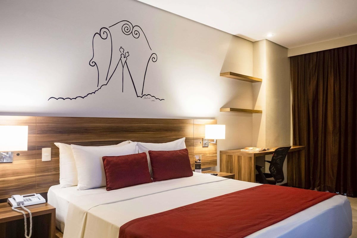 A hotel room with a bed, bedside lamps, a desk, and a telephone.