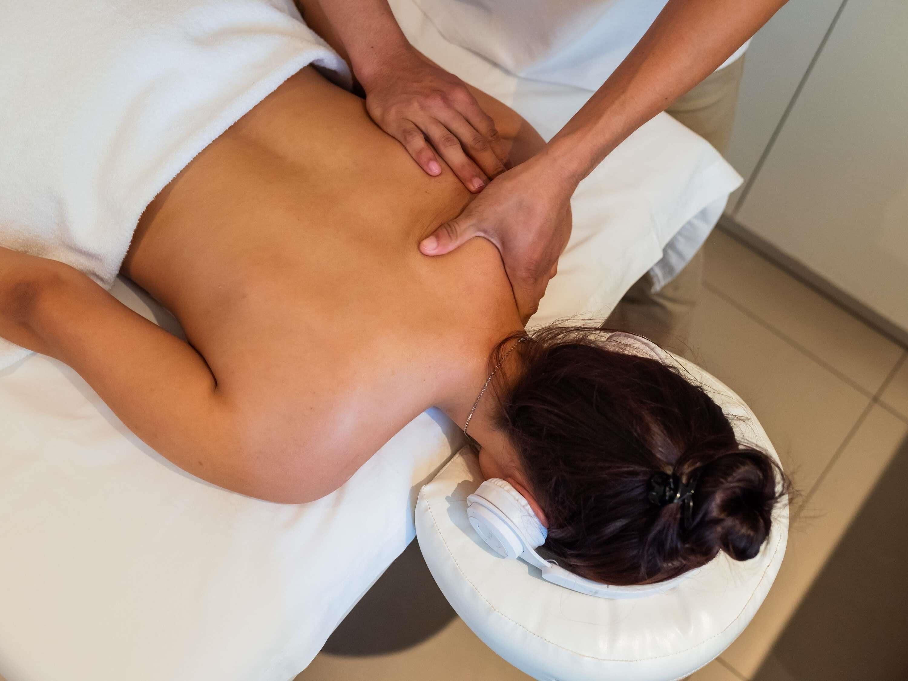 Uma pessoa recebendo uma massagem nas costas em um quarto com uma cama branca e uma cadeira branca.
