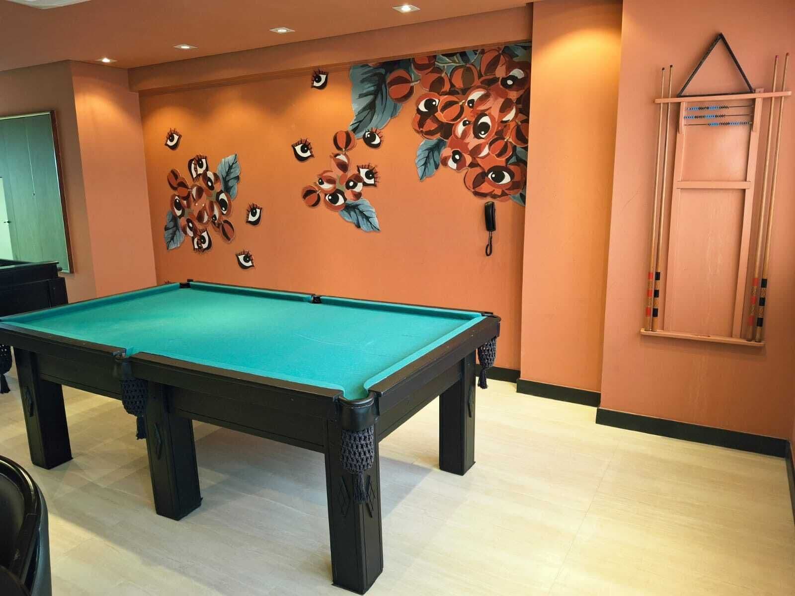 Uma mesa de bilhar em um salão com paredes laranja e um mural de olhos e folhas.