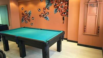 Uma mesa de bilhar em um salão com paredes laranja e um mural de olhos e folhas.