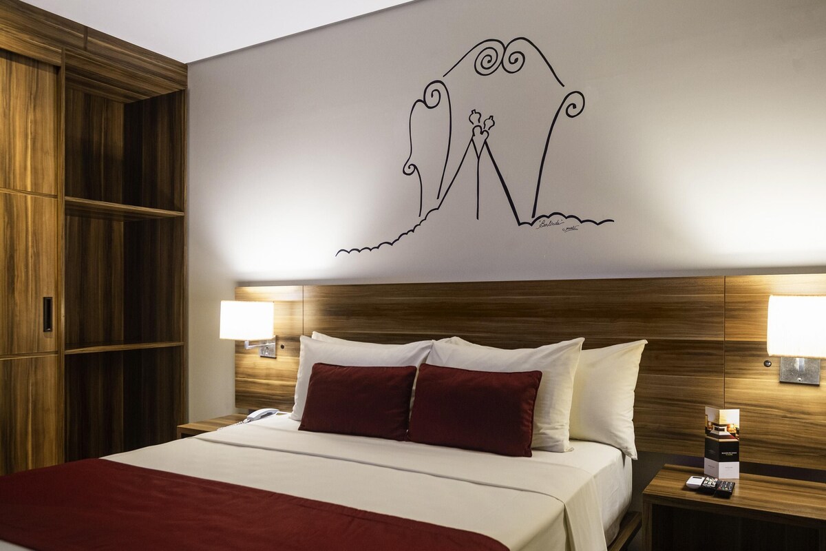Une chambre d’hôtel avec un grand lit, une tête de lit en bois, deux lampes de chevet et un élément décoratif mural.