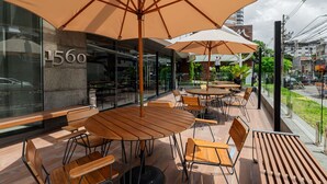 An outdoor seating area with wooden tables and chairs, large umbrellas, and a view of the street. - Mercure Belém Boulevard (Belém)