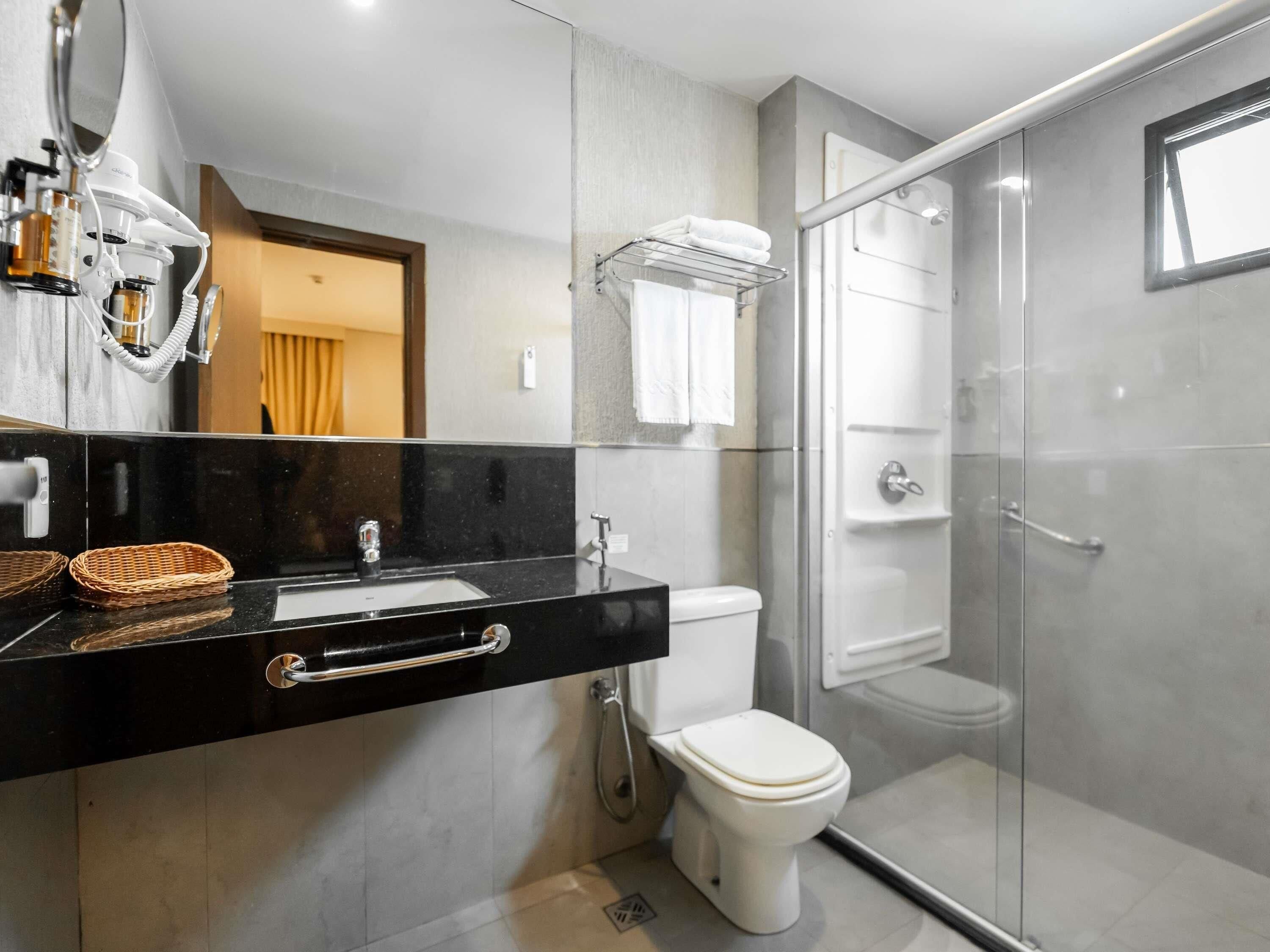 A modern bathroom with a black countertop, a white toilet, a glass shower enclosure, and a mirror with a towel rack above it.