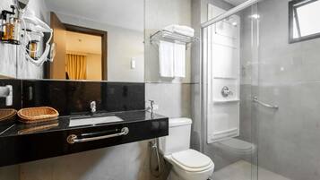 A modern bathroom with a black countertop, a white toilet, a glass shower enclosure, and a mirror with a towel rack above it.